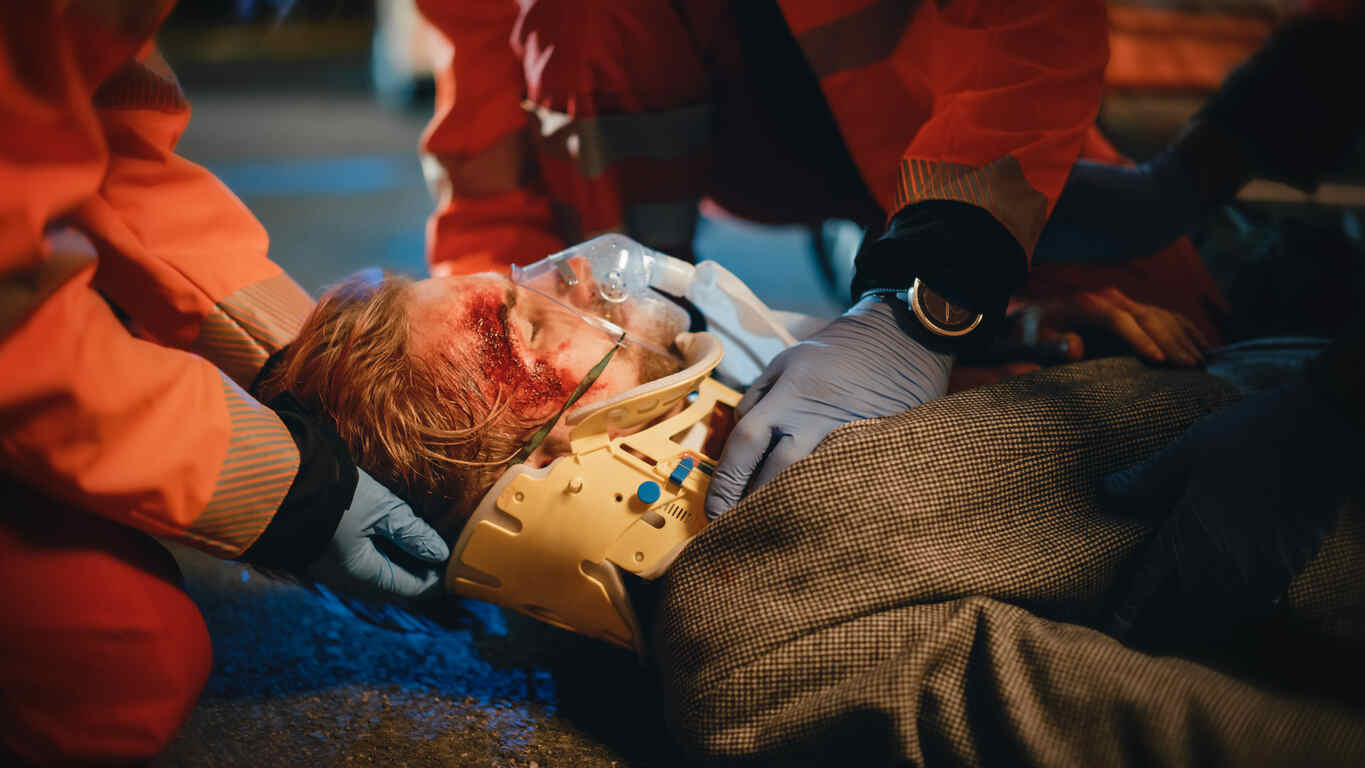 Emergency responders providing medical care to a man with a severe head injury and neck brace after a rear-end collision in Virginia, highlighting catastrophic injuries beyond whiplash.